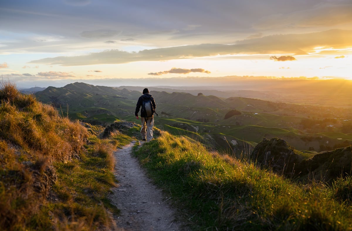 Man hiking on top of the hill. Setting sun casting a warm glow on rolling hills.